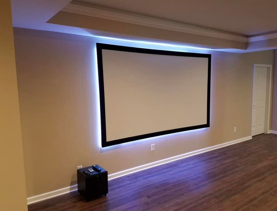 Home theater screen with black frame and blue LED lighting, mounted on a tan wall.
