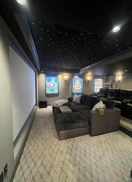 Home theater with a large screen, dark couch, starry ceiling, movie posters, and patterned carpet.