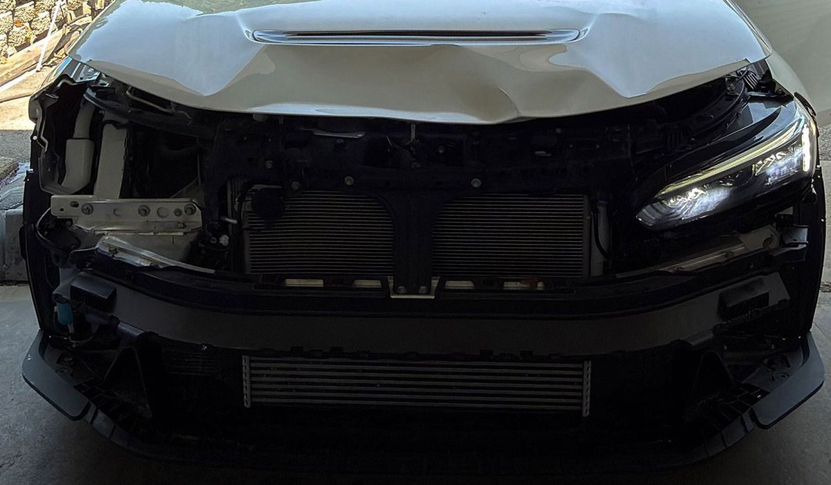 Front view of a black car with a damaged front bumper and grille in a garage-like setting