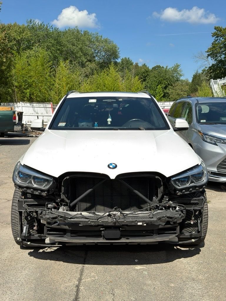 Front view of a white BMW with severe front-end damage in a parking lot.