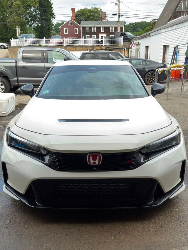 Front view of a white Honda Civic parked in a driveway with other cars and houses in the background