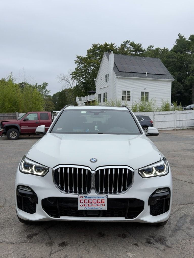 White BMW SUV parked in a lot with a house and red truck in the background