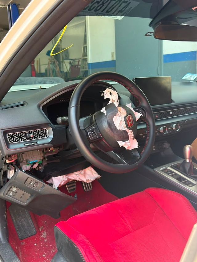 Car interior with a black dashboard, red seat cover, and a partially detached steering wheel cover.