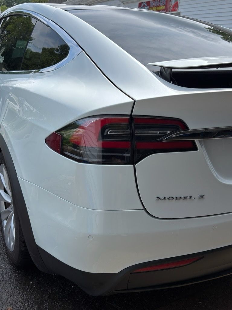Rear view of a white Tesla Model X parked on a street, showing the left taillight and rear hatch