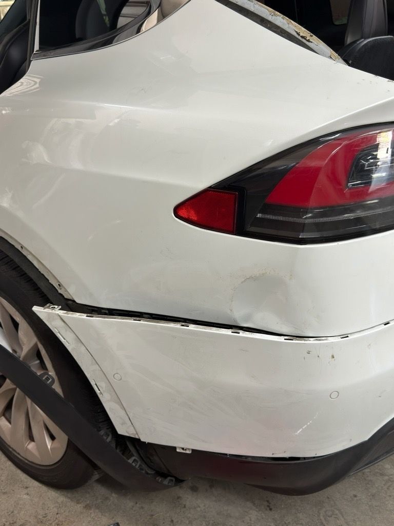 Rear side of a white car with a scuffed, cracked bumper near the taillight
