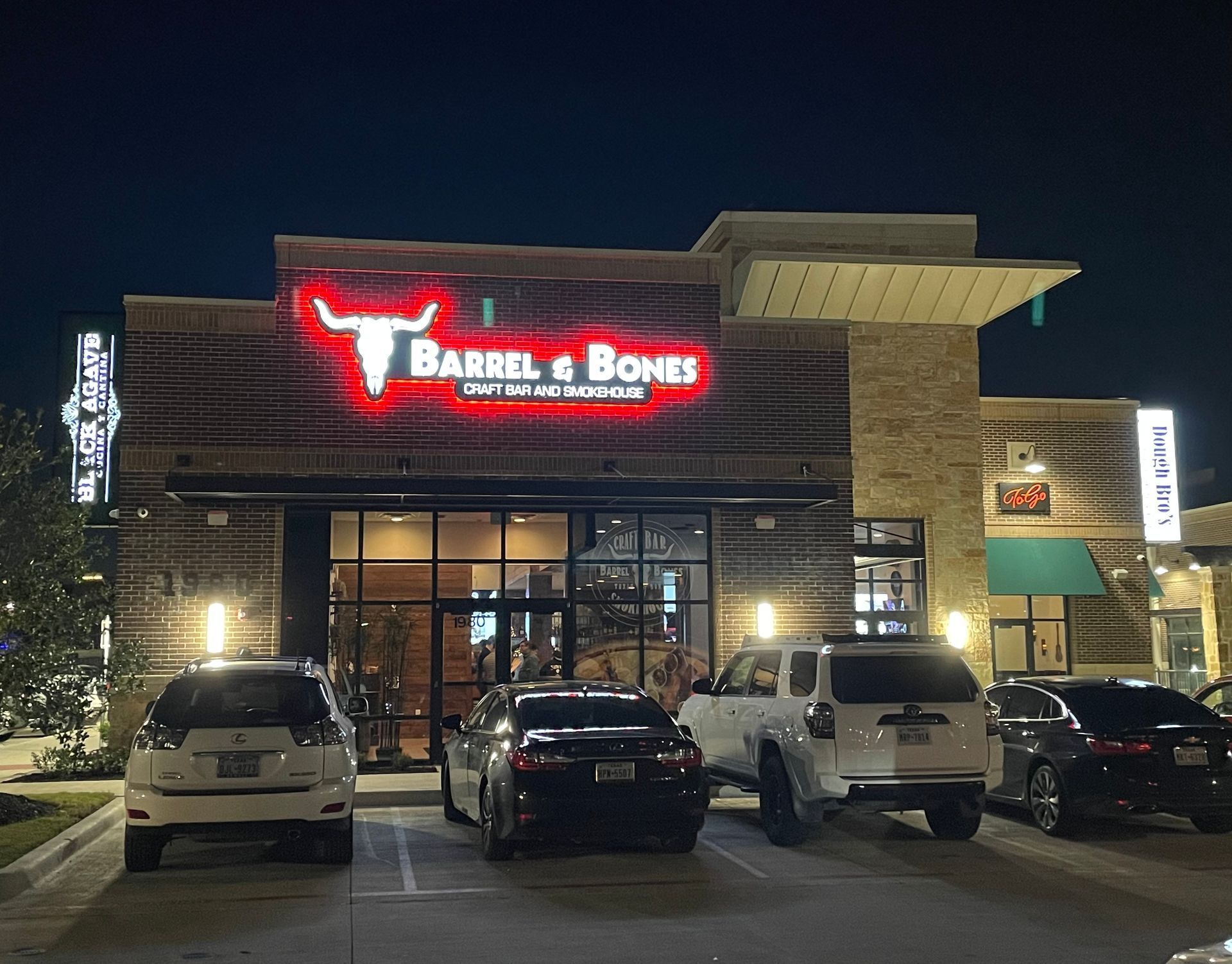 Barrel & Bones restaurant exterior at night with lit sign and parked cars.