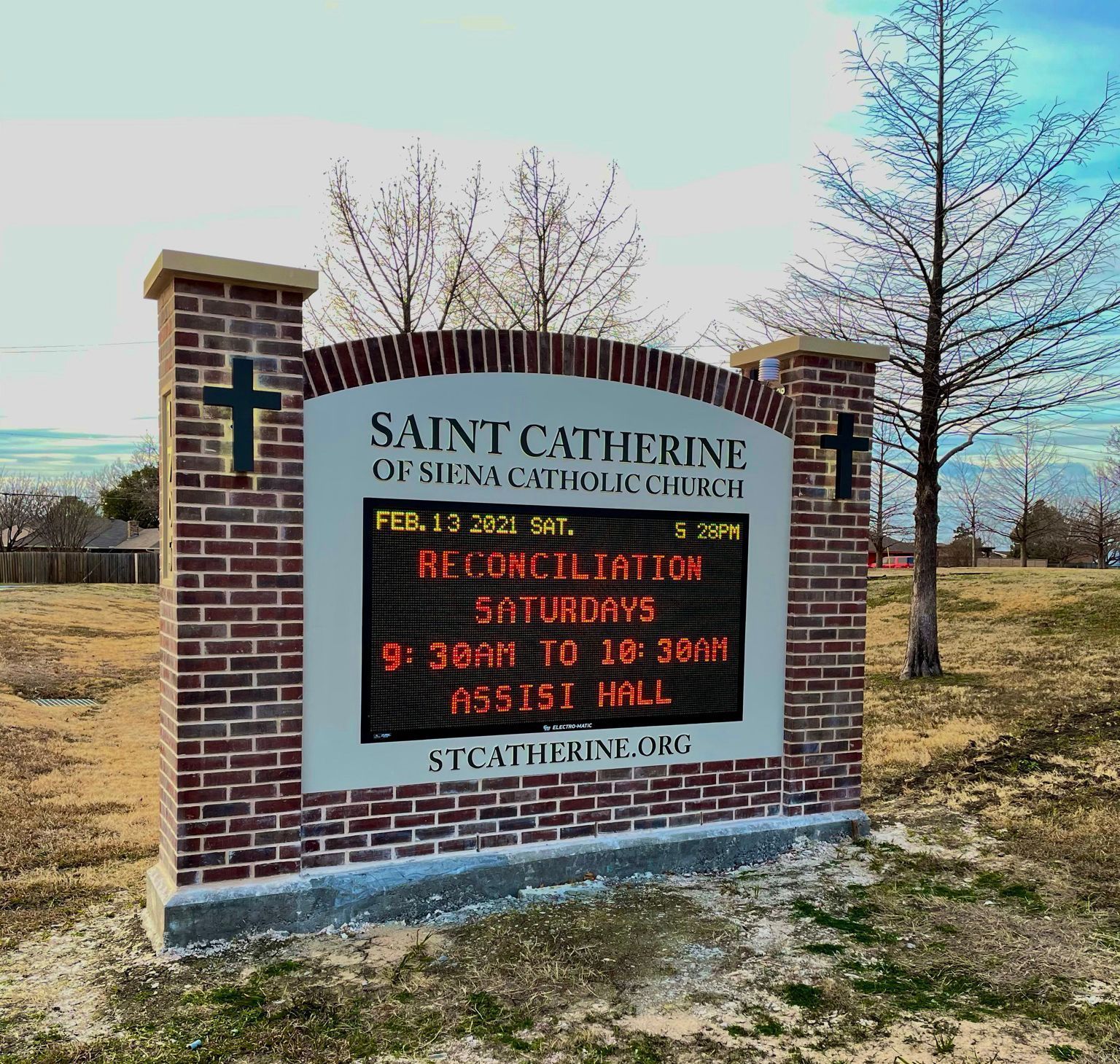Sign for Saint Catherine of Siena Catholic Church, brick and light, displaying reconciliation times on Saturdays.