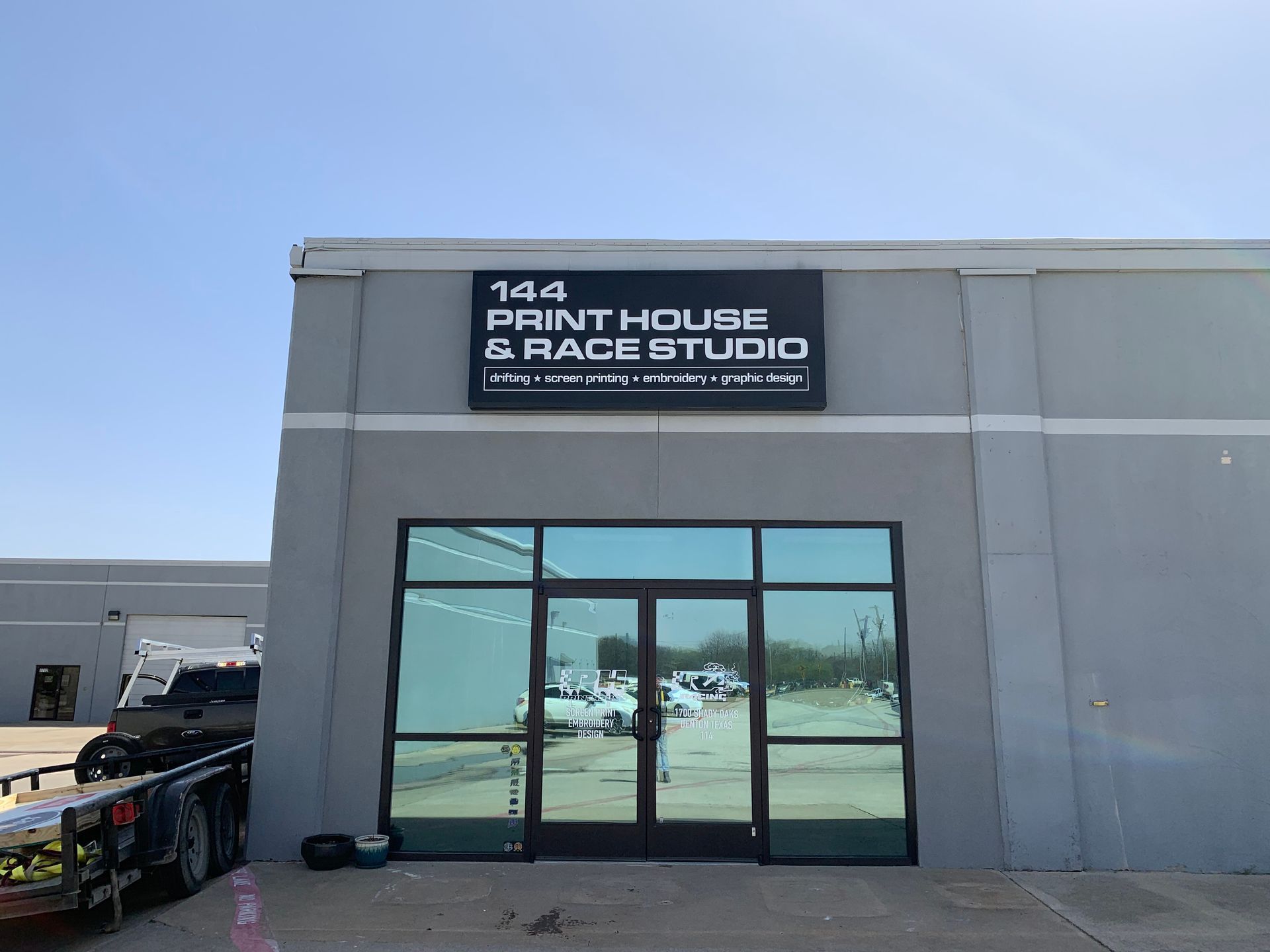 Exterior of a gray building with a “144 Print House & Race Studio” sign and glass double doors