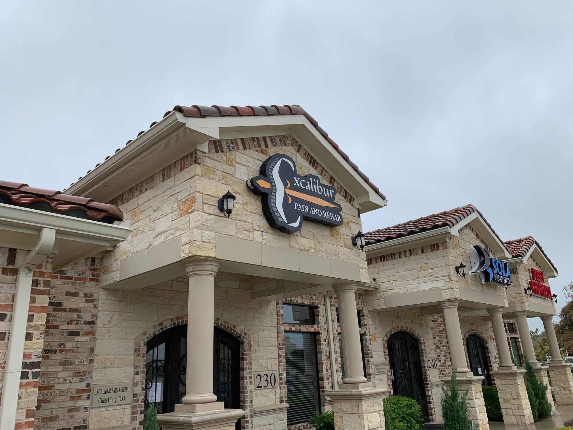 Stone storefront with arched columns and a colorful sign under a cloudy sky