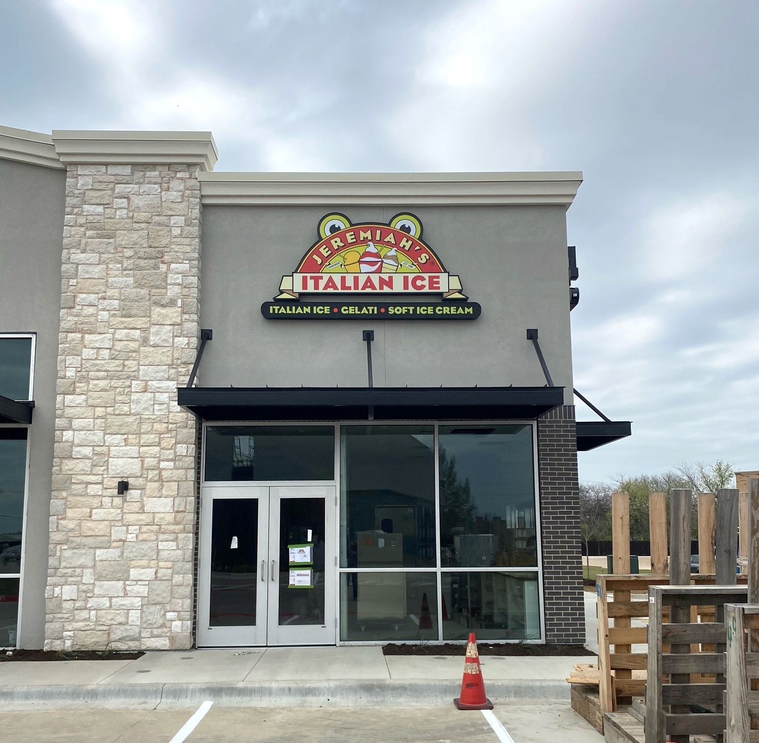 Storefront with sign for Itz Aizza Italian Ice, stone facade, glass doors, and a cloudy sky