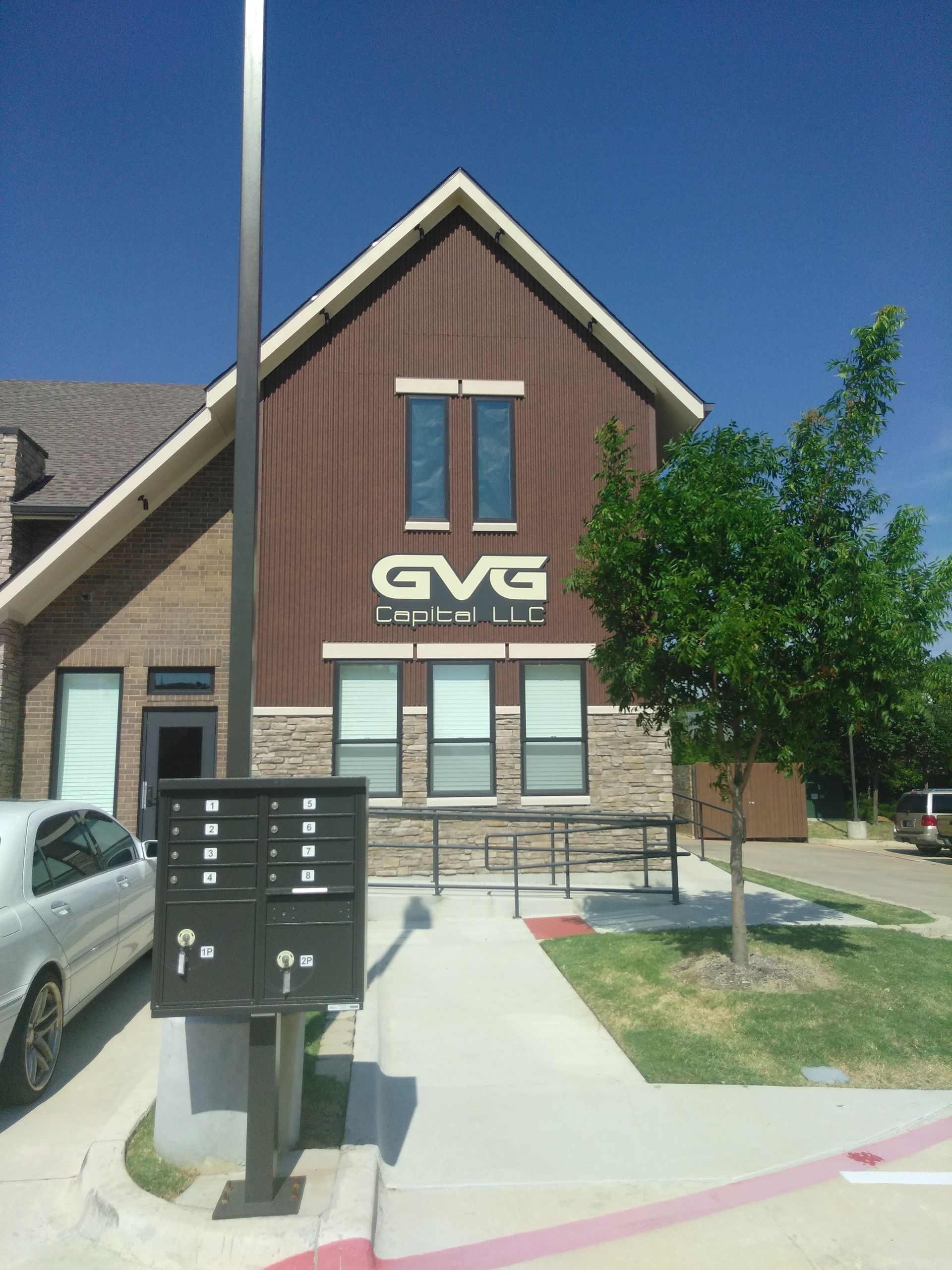 Brick building with GVG sign, front steps, mailbox, and parked car under a blue sky