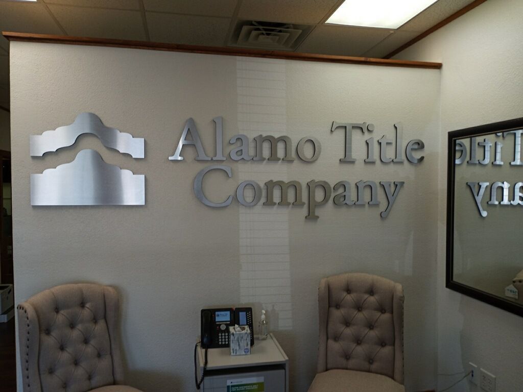 Alamo Title Company lobby with wall logo, mirror, and two gray chairs under fluorescent lighting