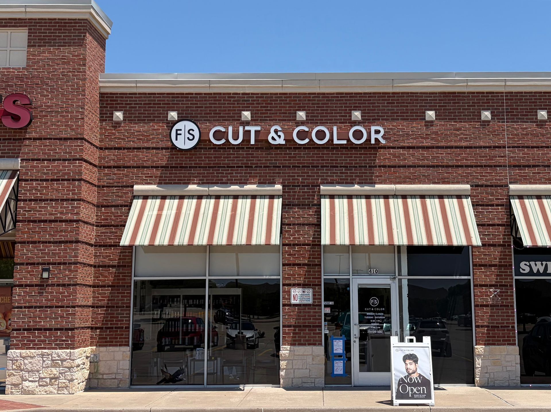 Storefront of a “Cut & Color” salon with striped awnings and brick facade
