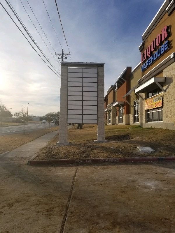 Multi-tenant pylon sign with blank tenant panels beside a commercial shopping center.