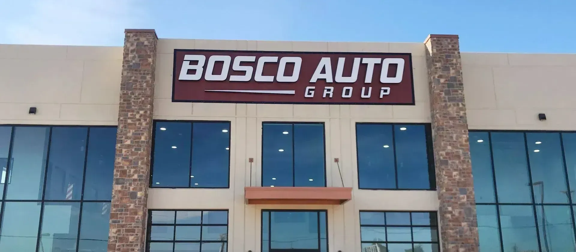 Bosco Auto Group storefront with stone columns and blue windows under a clear sky.