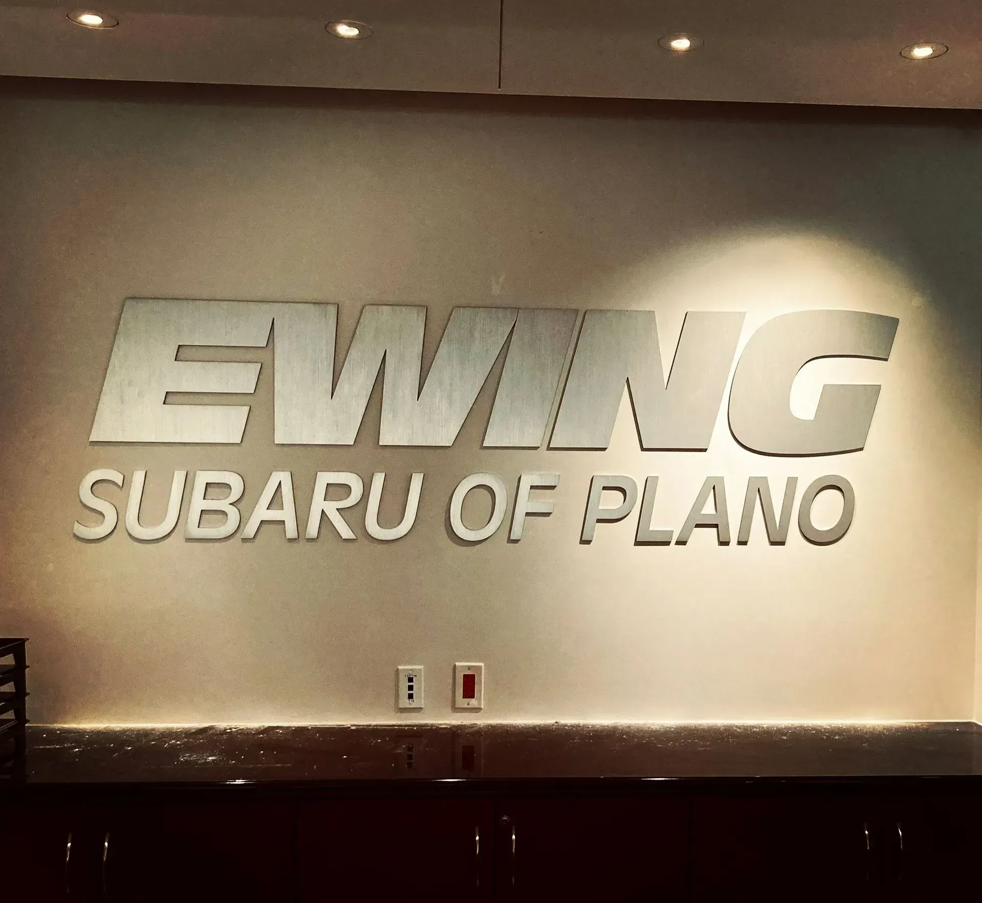 EWING Subaru of Plano sign on a wall in a showroom lobby.