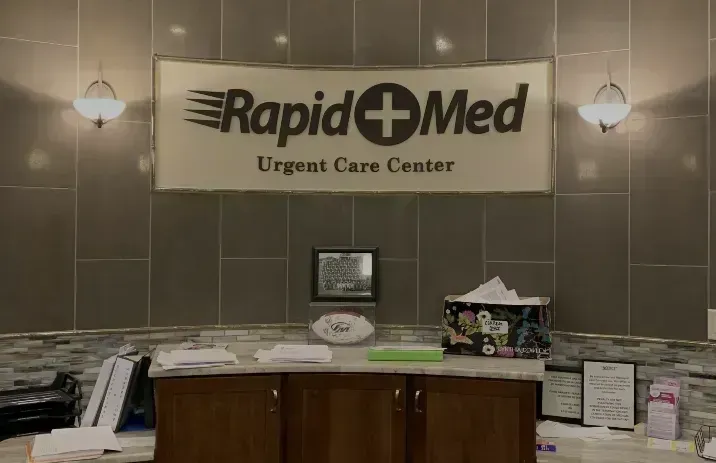 RapidMed Urgent Care Center reception desk with sign, brochures, and wall lamps.