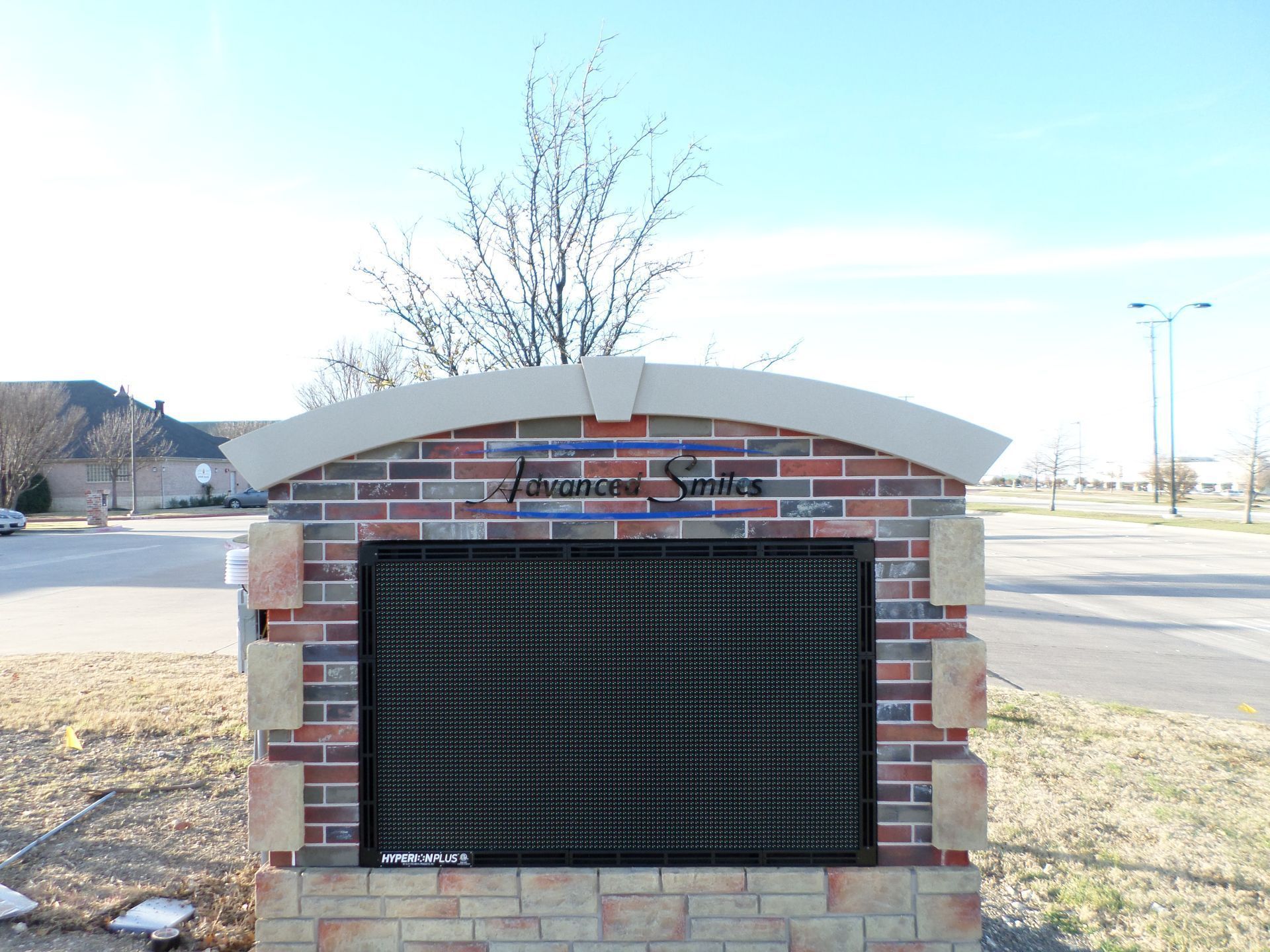 Brick community monument sign with dark LED display beside a road on a sunny day