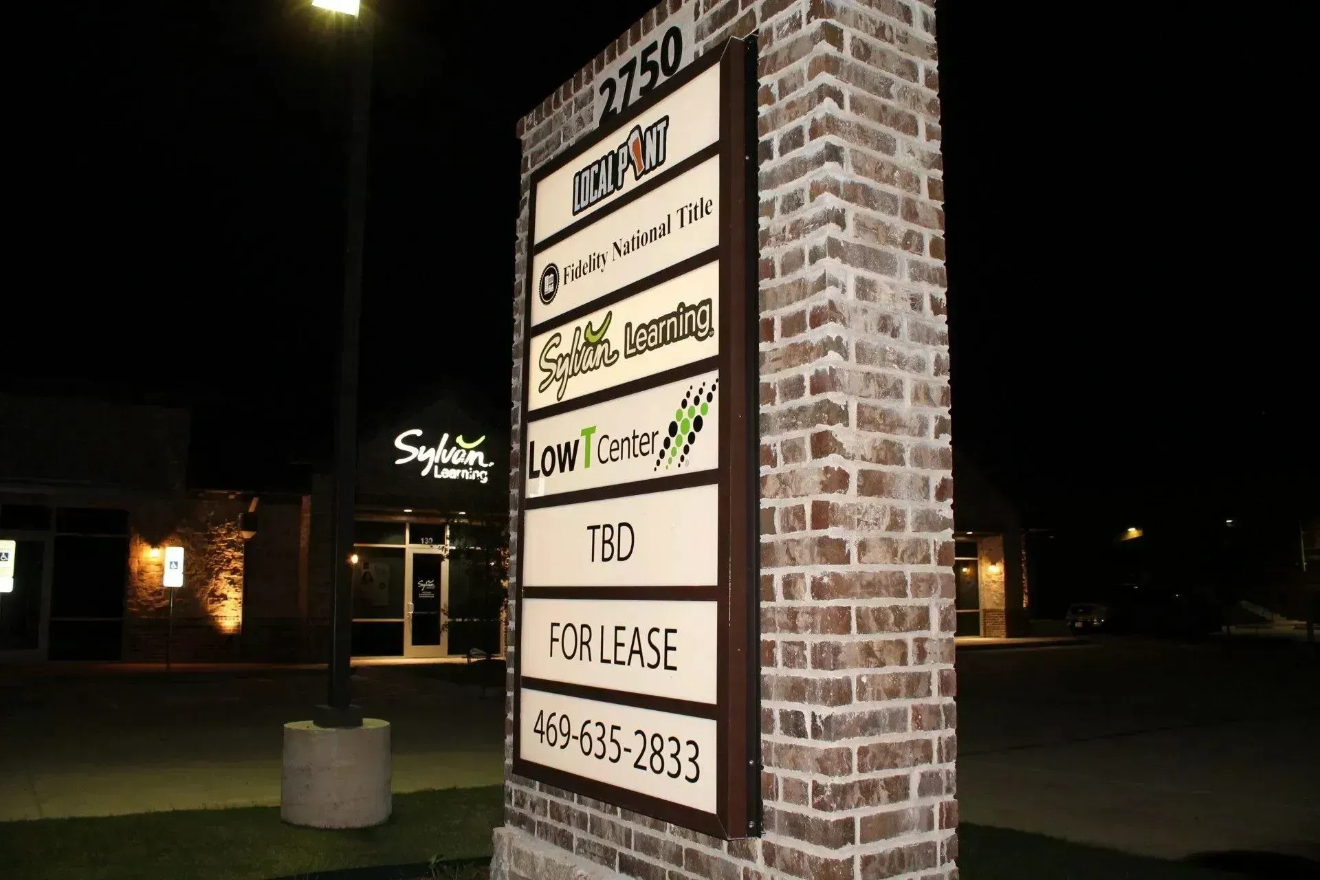 Brick sign for a strip mall listing business names at night under bright lights