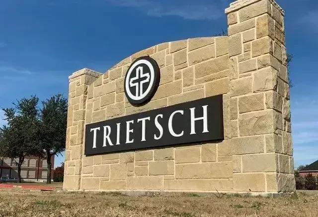 Sign for Trietsch Church, tan stone with black sign that includes the church's name and logo on a sunny day.