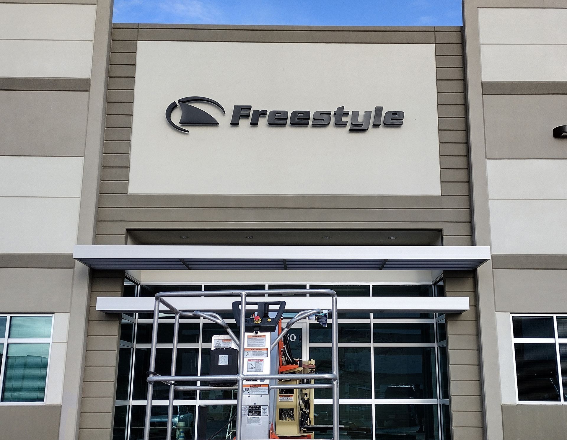 Freesstyle storefront with a worker on a lift installing signage above the entrance