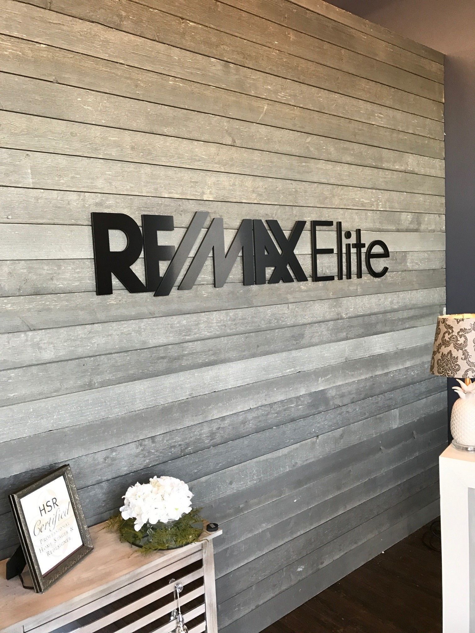 RE/MAX Elite office wall sign above a small table with flowers and decor