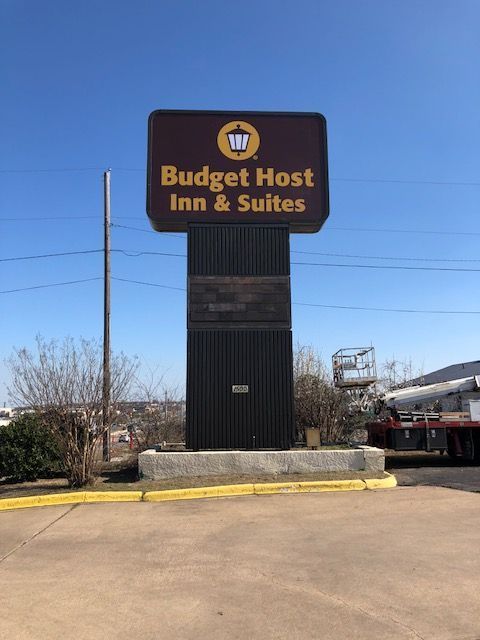 Budget Host Inn & Suites sign on a tall black post in a parking lot under a blue sky
