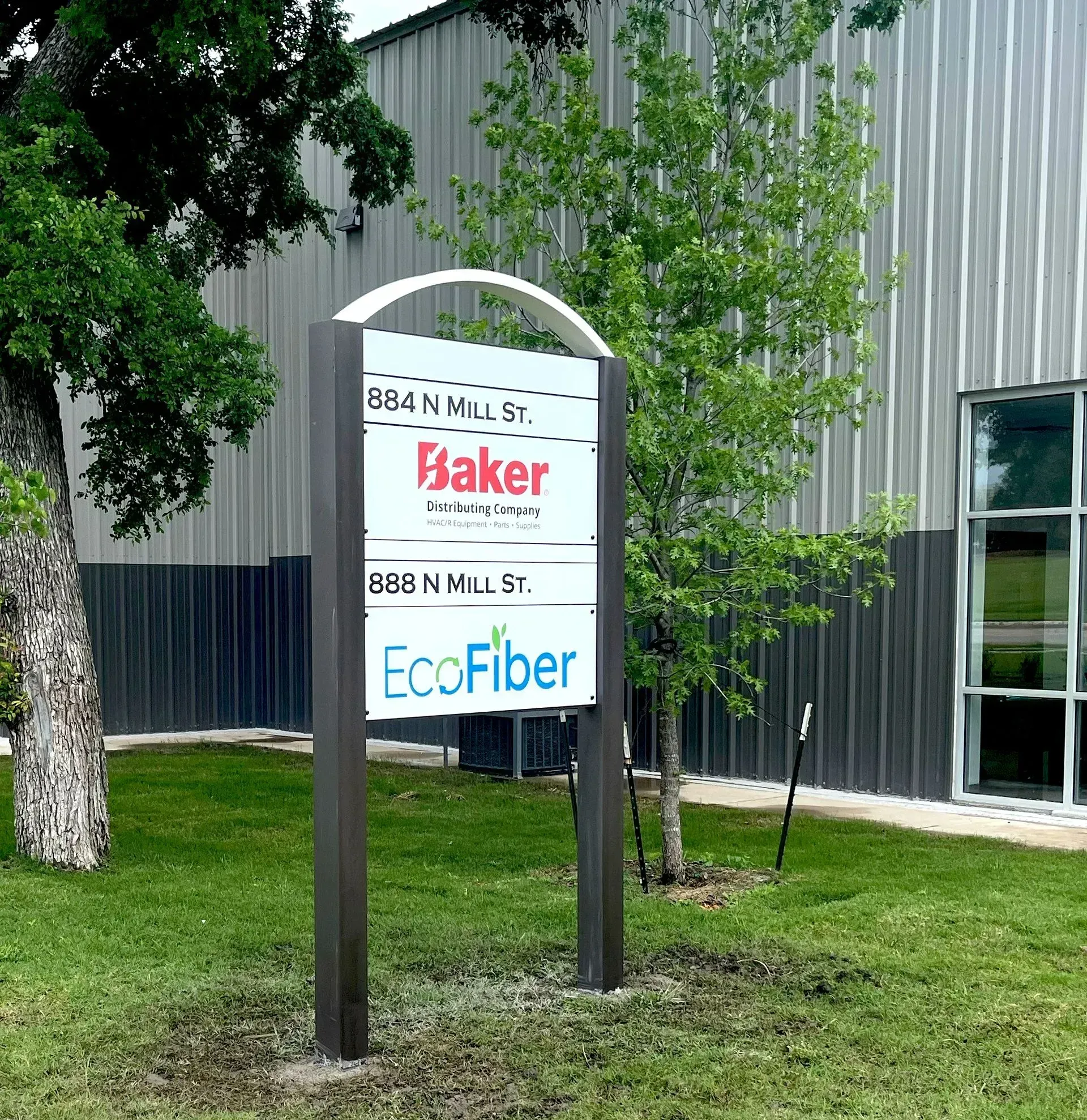Sign at Baker and EcoFiber outside a metal building with trees and grass