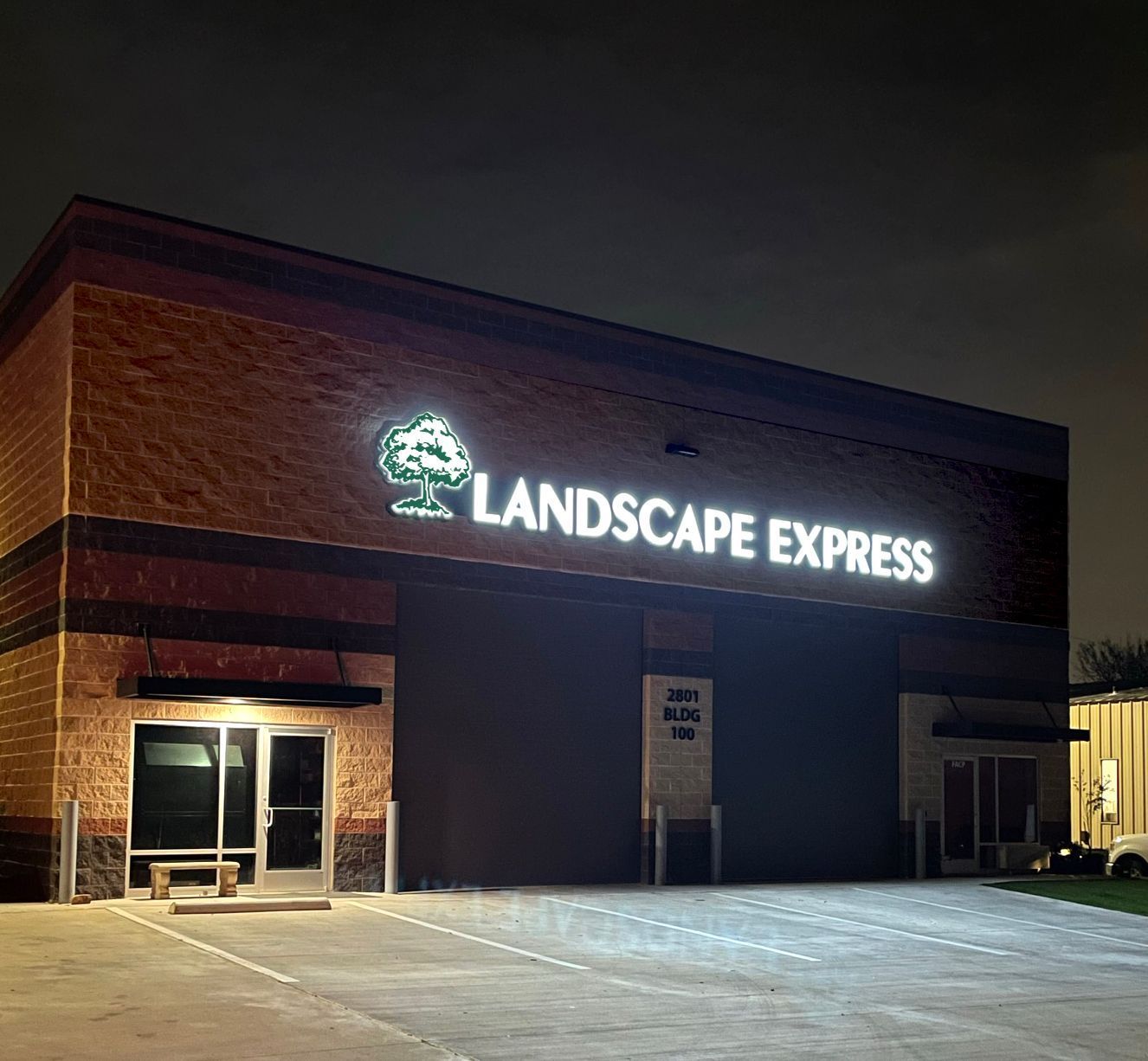 Illuminated channel letter sign and tree logo for Landscape Express on a commercial building at night.
