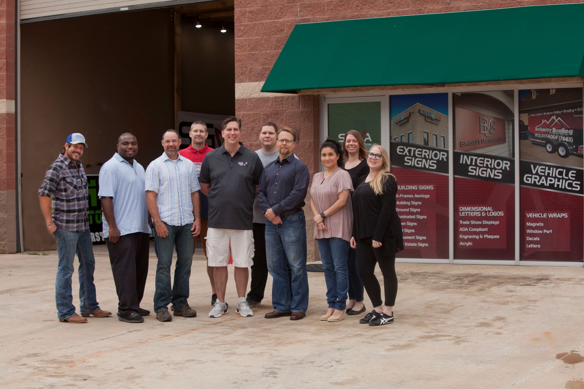 Group of people standing in front of a building with signs. Brick wall, green awning, sunny day.