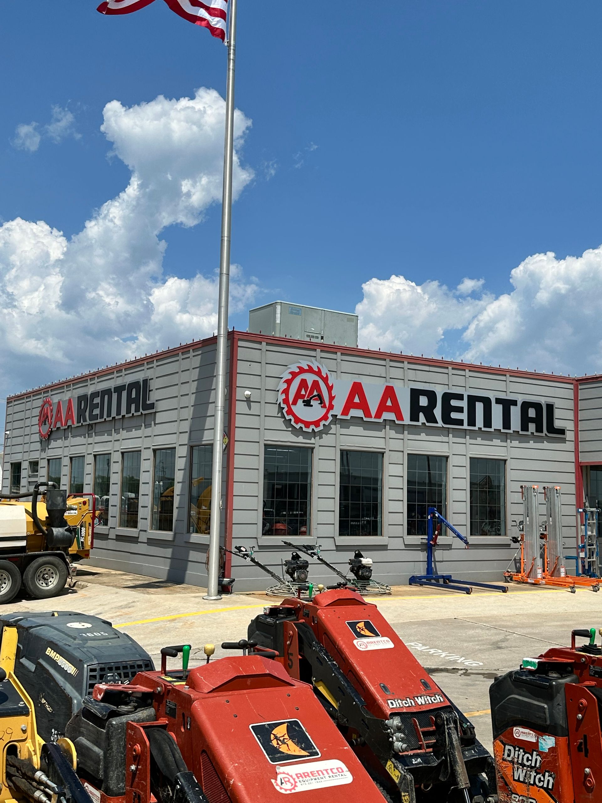 AA Rental store with construction equipment in front and American flag.