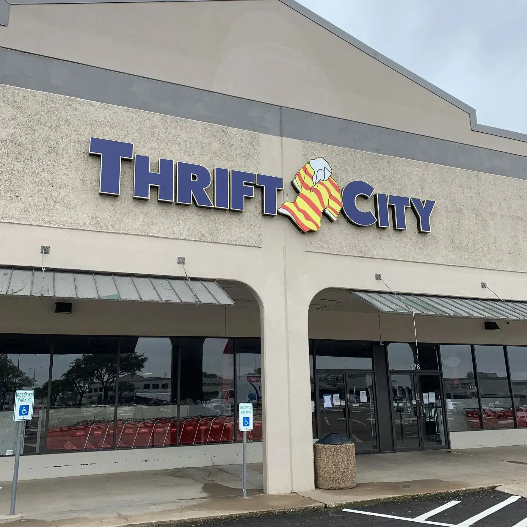 Thrift City store with blue and gold sign. Gray building with windowed entrance, and parking.