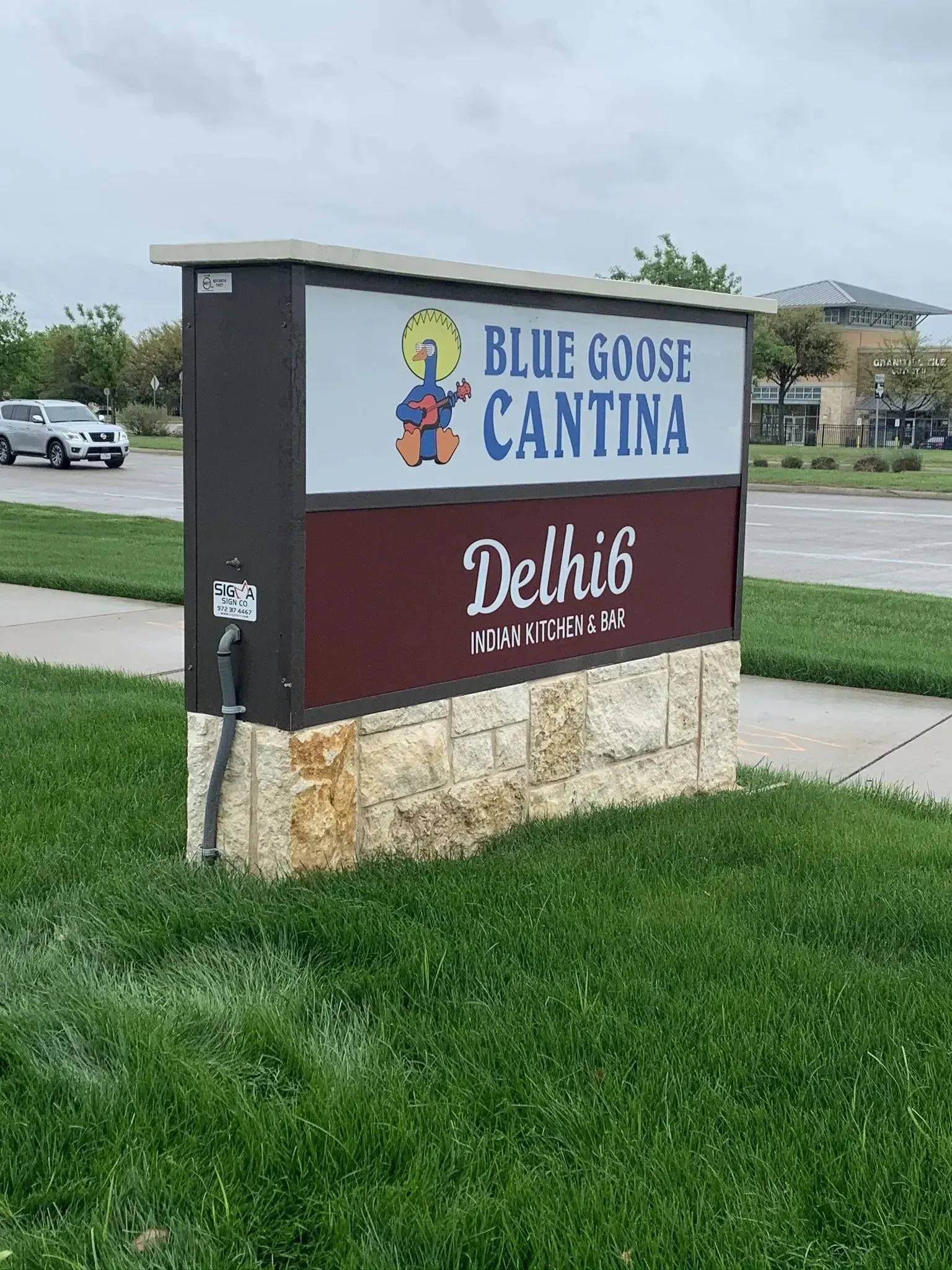 Sign for Blue Goose Cantina and Delhi6 restaurants with logo on a grassy median.