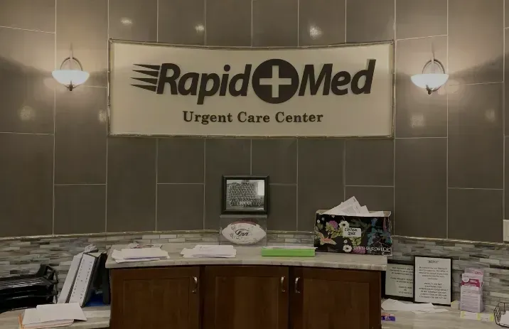 RapidMed Urgent Care Center reception desk with logo, brown cabinets, and paperwork.