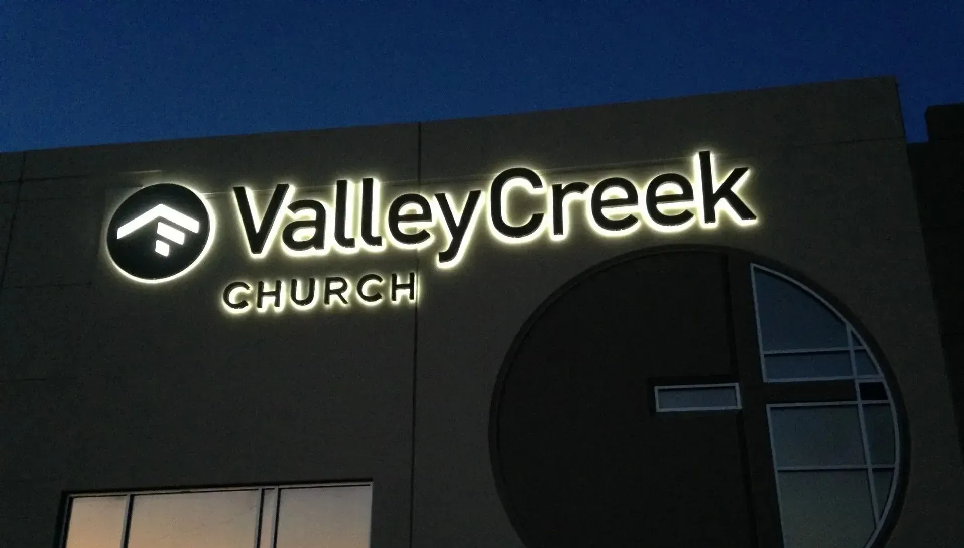 Illuminated sign for ValleyCreek Church on a building facade; includes logo with an upward arrow and cross.