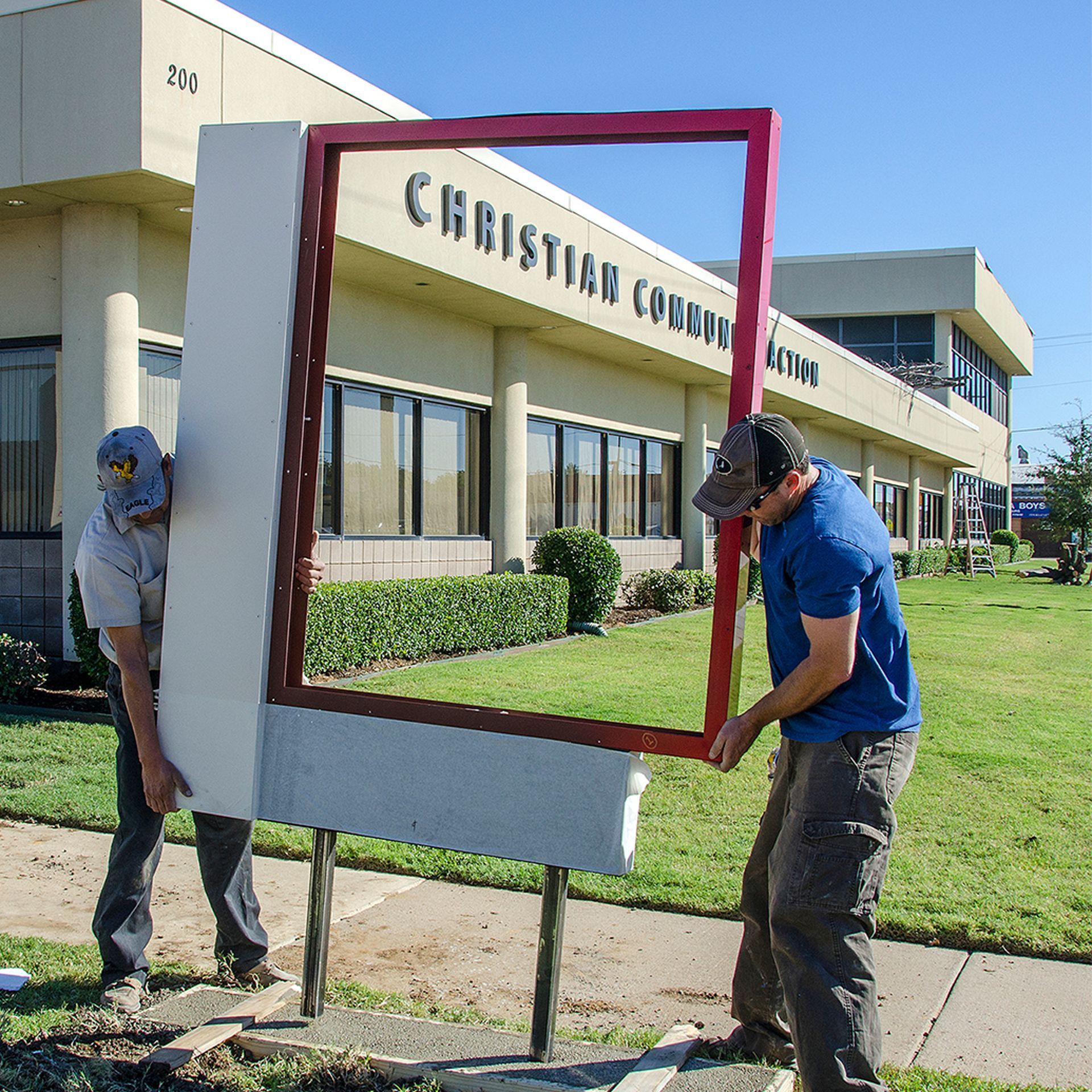 Two workers carrying a red frame in front of a Christian college building