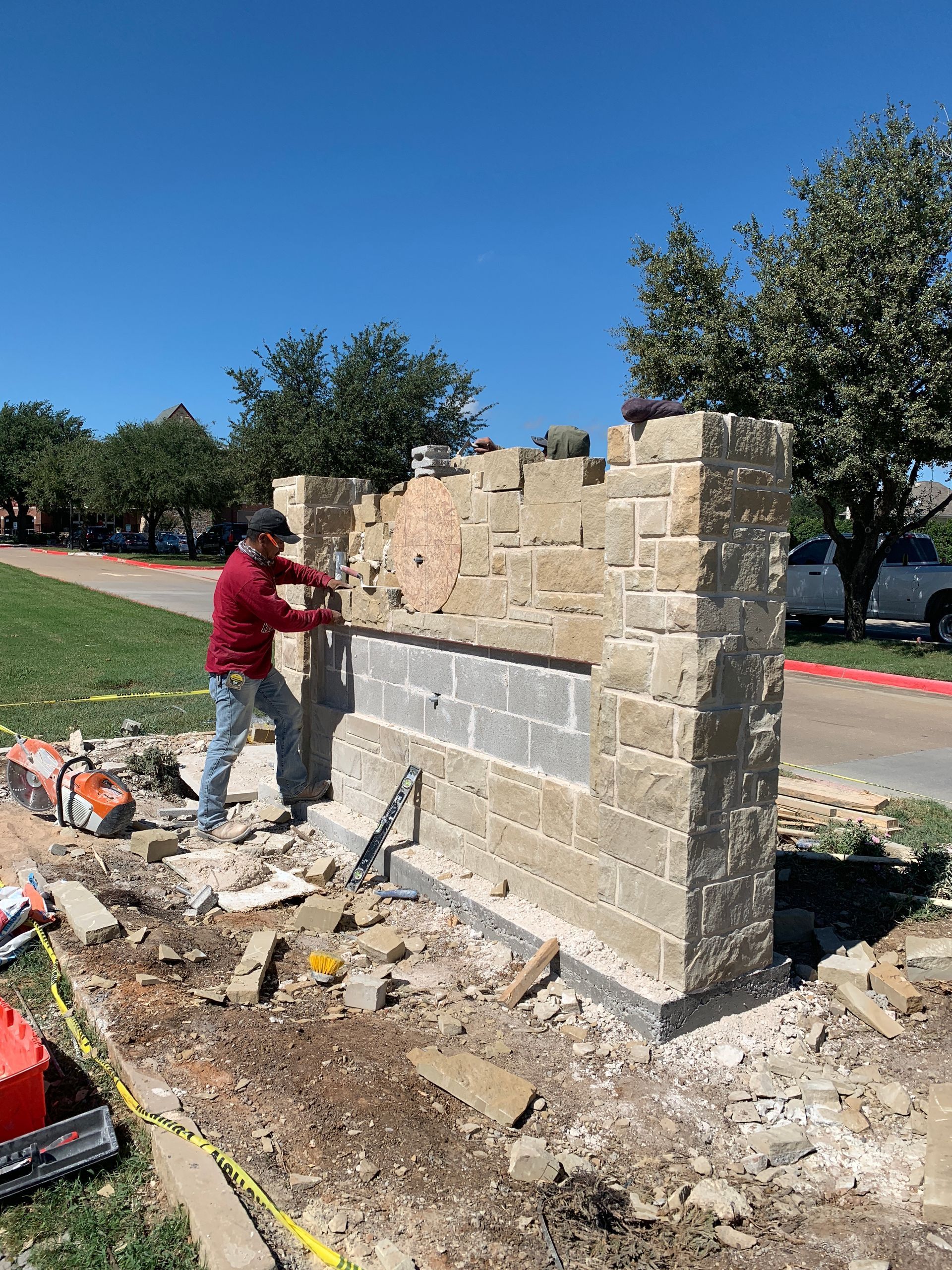 Worker building a stone wall beside a sidewalk on a sunny day