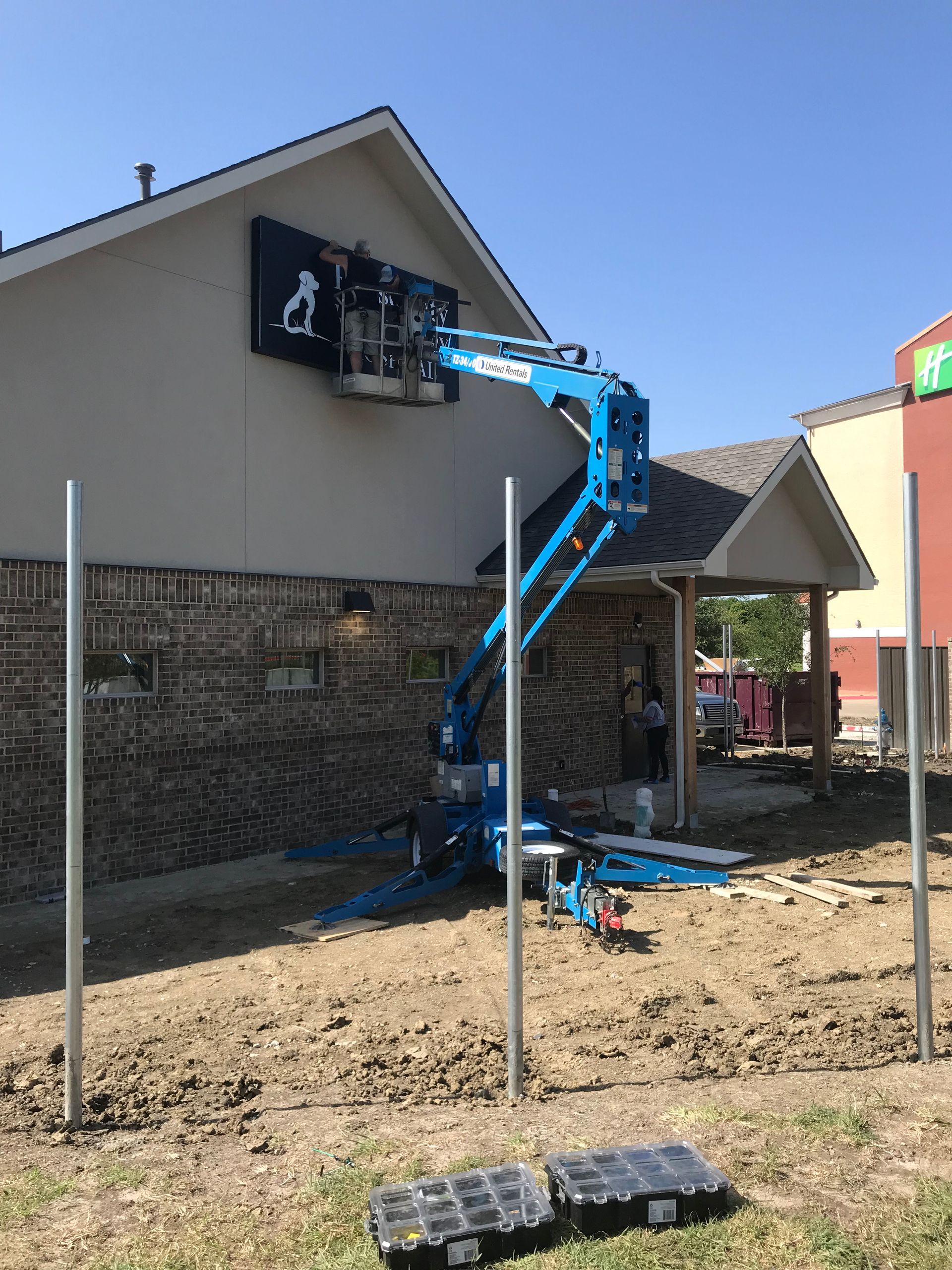 Worker in a blue lift repairing a black sign on a building exterior.