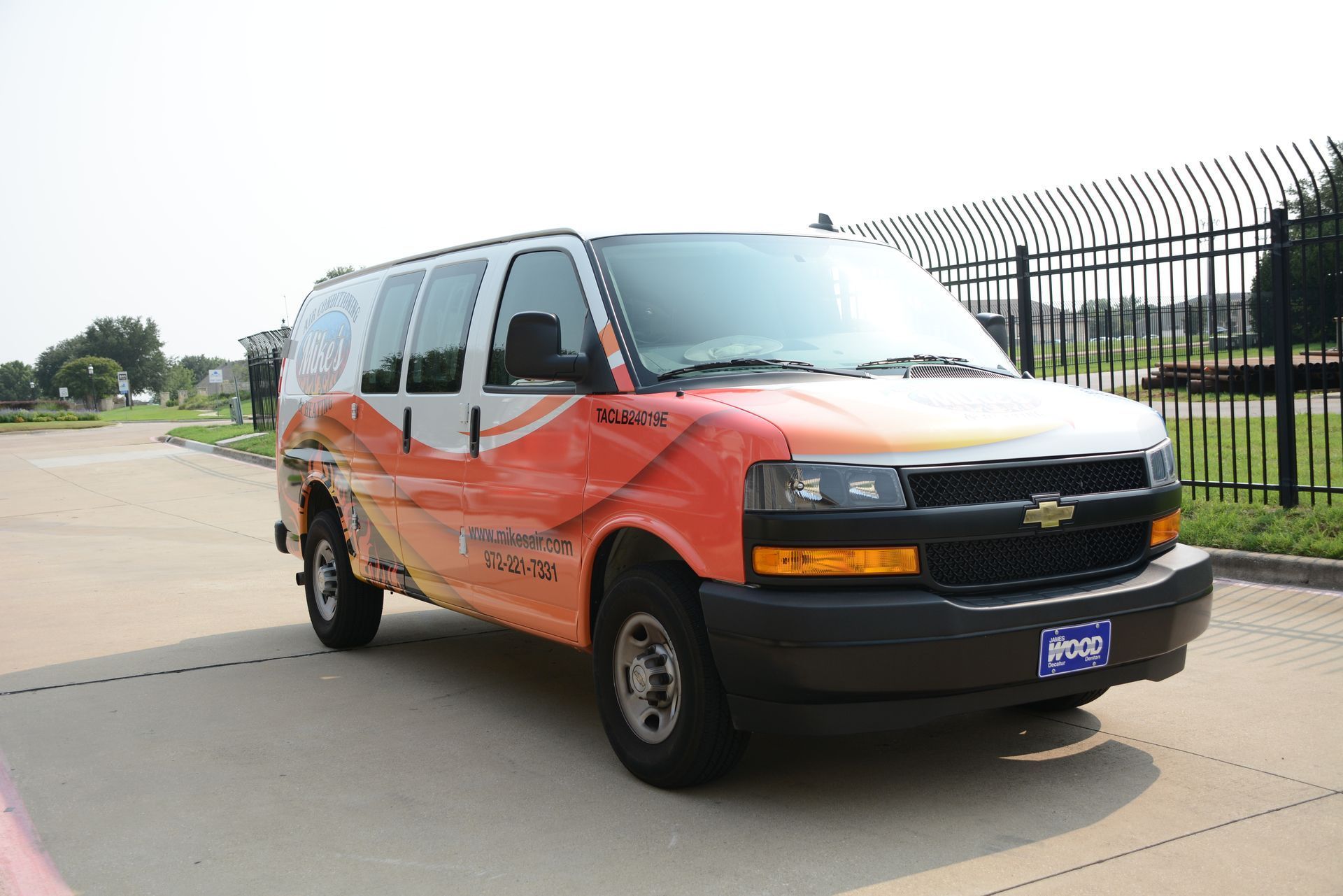 Orange and white Chevrolet van parked on a paved road beside a fence