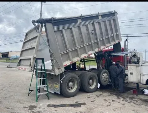 Dump truck with raised bed, mechanics working on the vehicle outdoors.