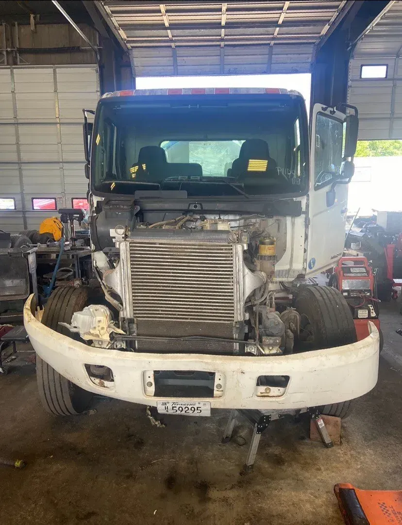 White truck front open, radiator exposed in repair shop.