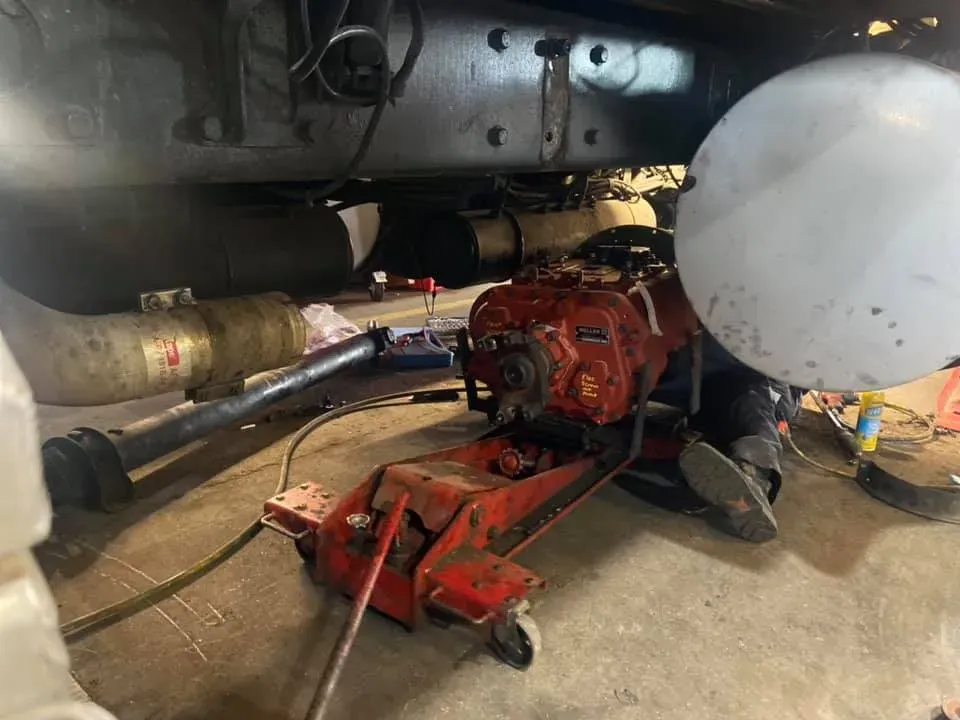 Red hydraulic jack supporting a red engine under a truck. Mechanics are working in a garage.