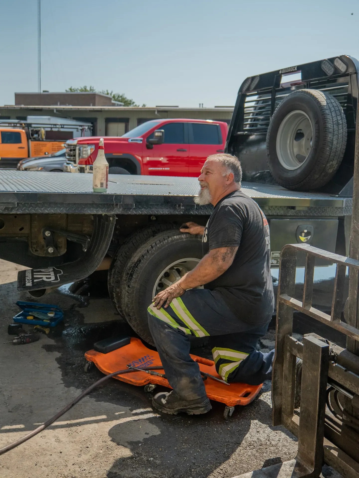 Mechanic works on a truck tire on a sunny day. He is kneeling on a creeper.