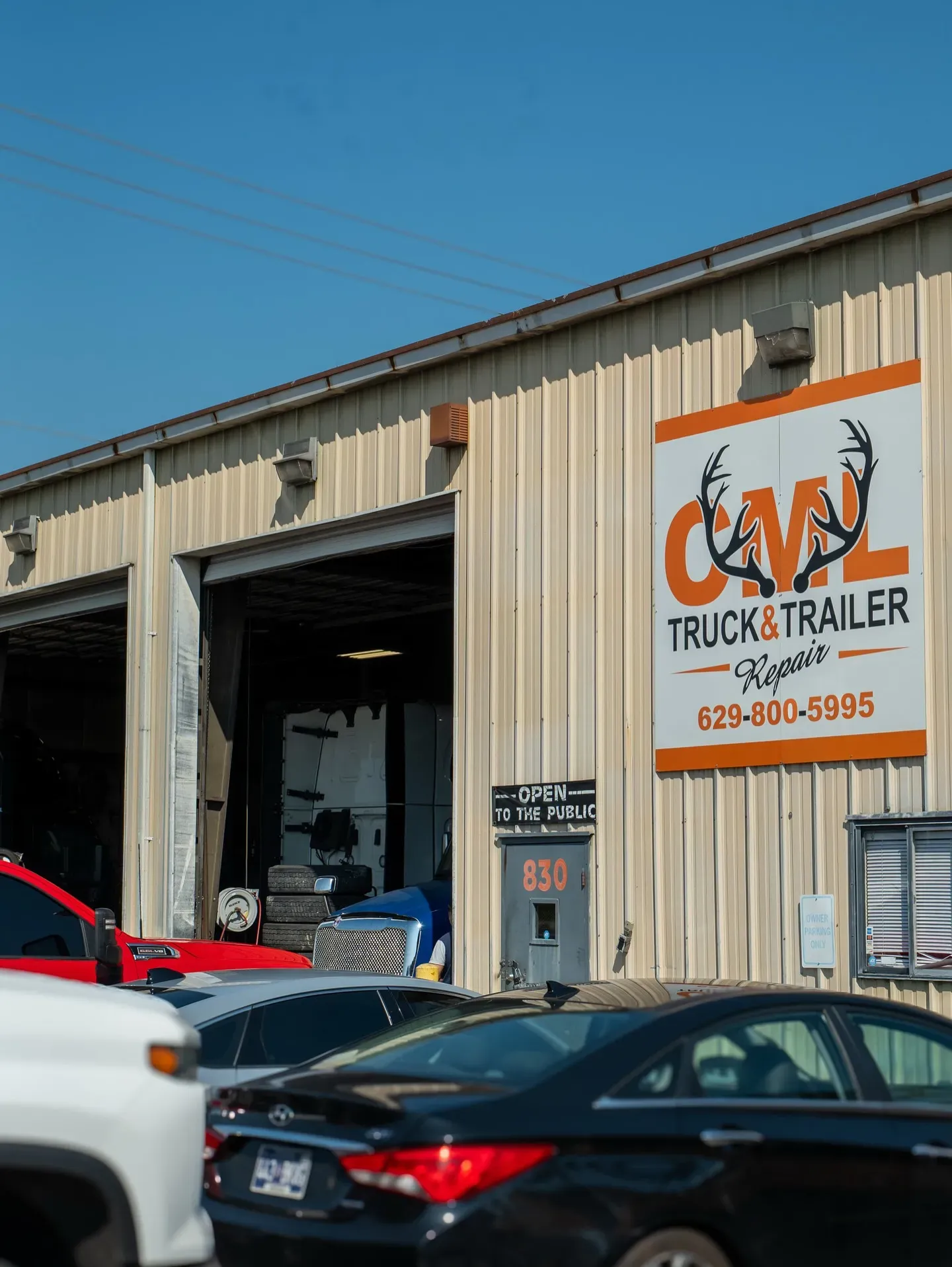 CML Trucks & Trailer building with an open bay door, parked vehicles in front, and a blue sky.