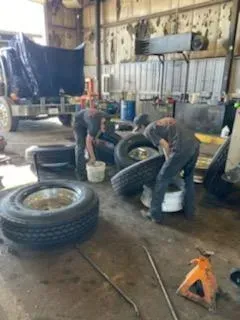 Two mechanics in a garage cleaning tires next to a truck.