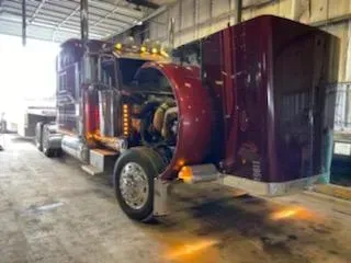 Red semi-truck with hood open in a repair shop, showing engine components.