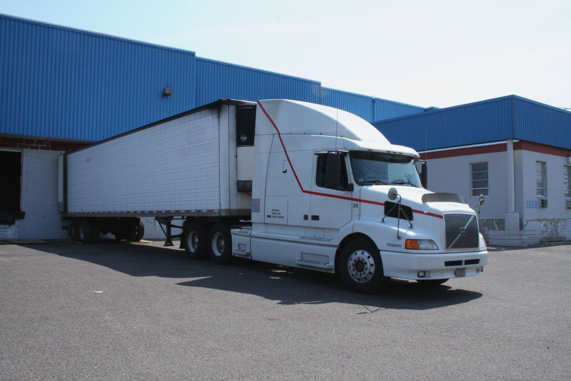 White semi-truck parked at a loading dock, preparing for loading or unloading at a blue warehouse.