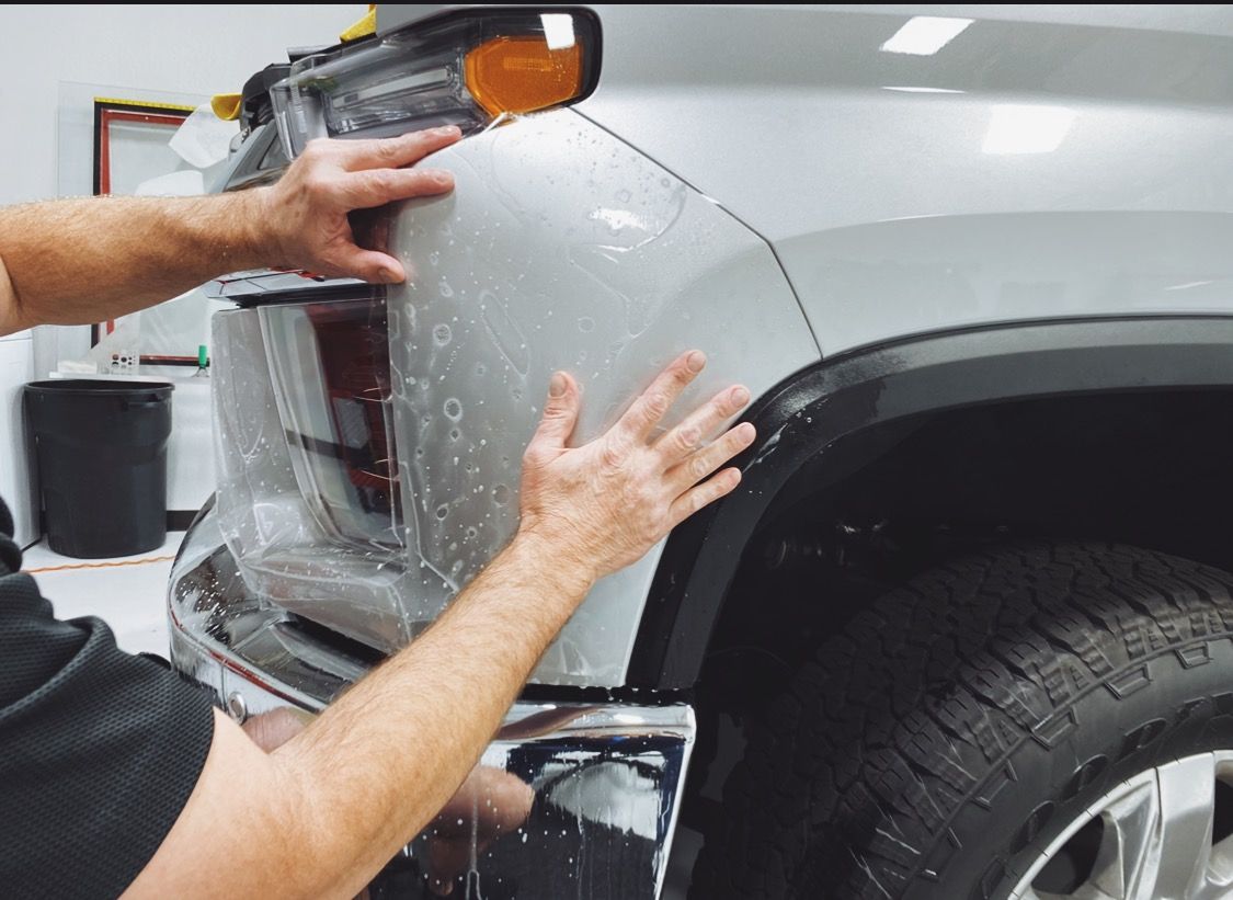 a man is applying a protective film to the front of a silver truck