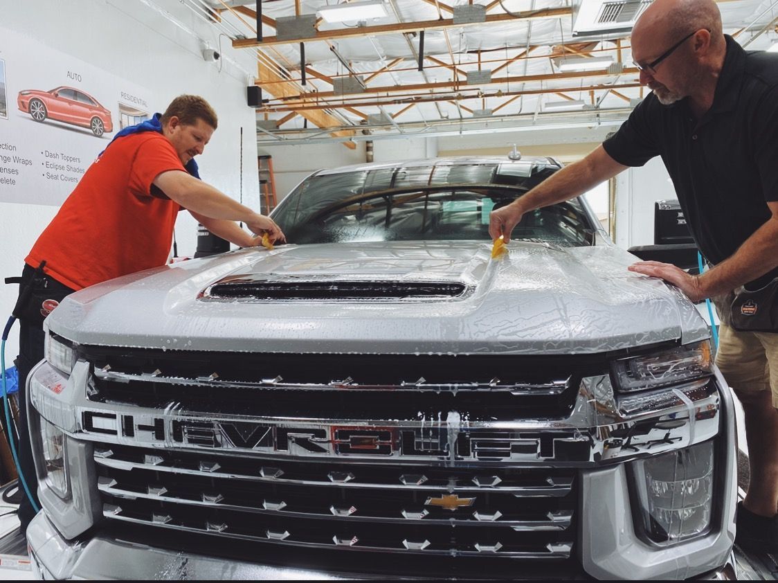 two men are working on the hood of a silver Chevrolet truck