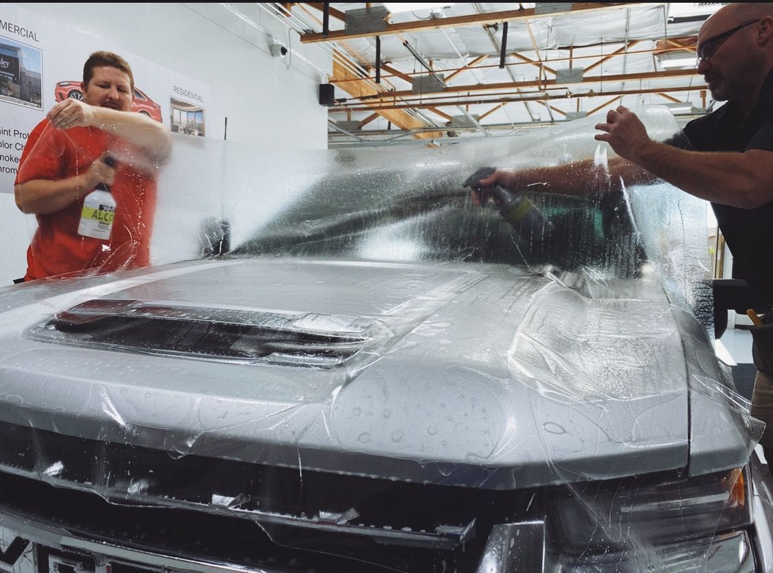 two men are wrapping a silver truck with plastic